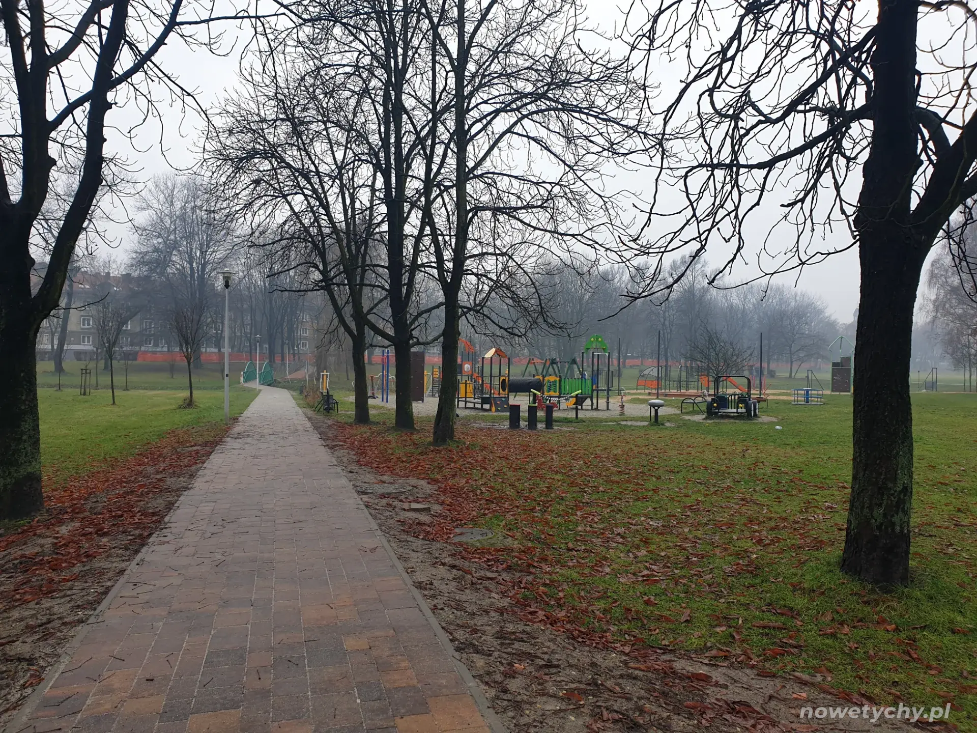 W tle plac zabaw i siłownia plenerowa